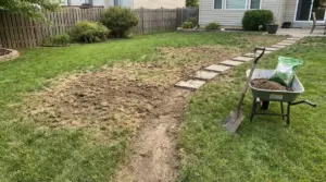 Zona del prato con erba diradata e chiazze secche durante il ripristino con terra e attrezzi da giardino