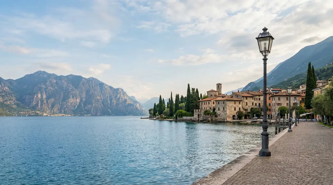Lungolago del Lago di Garda con borgo sullo sfondo, lampione e montagne, in una giornata tranquilla